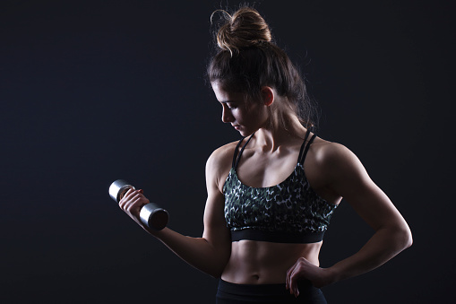 Athletic woman exercising with dumbbells on black background