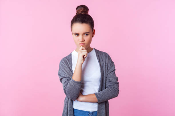 portrait of smart pensive brunette teenage girl holding hand on chin and thinking. indoor studio shot isolated on pink background - pensive question mark teenager adversity imagens e fotografias de stock