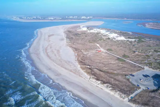 Aerial view from over the water of Oak Island point looking toward Holden Beach. The waves are crashing onto the beach. View of the tip of the Island.