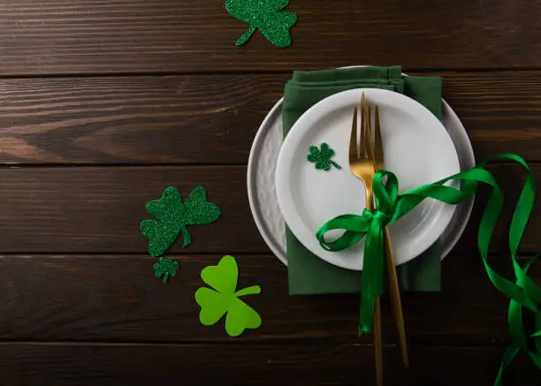 Photo of St. Patrick's Day green Shamrocks with fork, spoon, and napkin on rustic brown wood board background with room or space for copy, text, words. Square