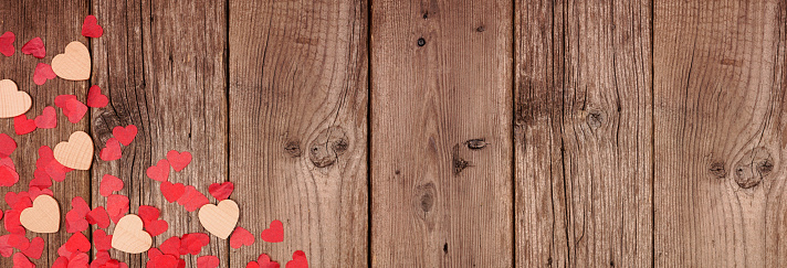 Valentines Day banner with corner border of wooden hearts and confetti. Top view on a rustic wood background. Copy space.