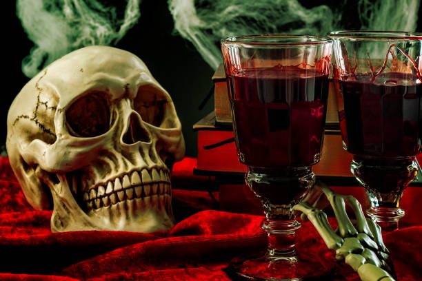 istock Halloween backdrop, haunted house and vampire drink conceptual idea with skull, glass filled with blood, spider webs, vintage books and skeleton arm on red velvet on black background 1198145937