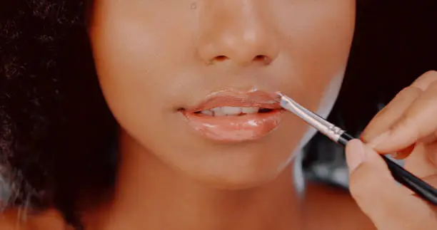 Cropped shot of a hand applying lipgloss to a beautiful young woman