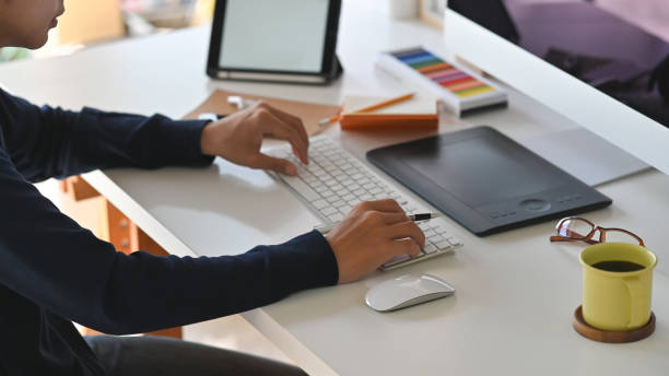 istock Side shot of young creative man while typing on the keyboard. Including Coffee cup, mouse, keyboard, color guide, tablet earphone, notebook and pencil on the work desk. 1198158946