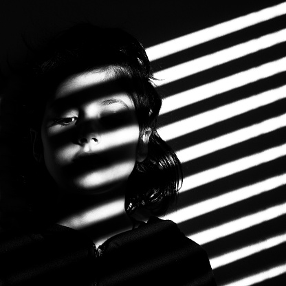 Girl partly illuminated by diagonal lines of light coming through blinds.
