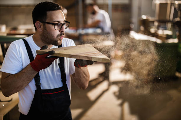 istock Young carpenter blowing sawdust from a plank. 1198179409