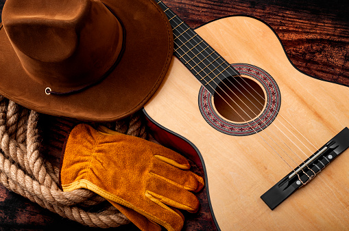 Cultura americana, vivir en un tema de concepto de rancho y música country con un sombrero de vaquero, guitarra acústica, guantes de granja y un lazo de cuerda sobre un fondo de madera en un antiguo salón photo