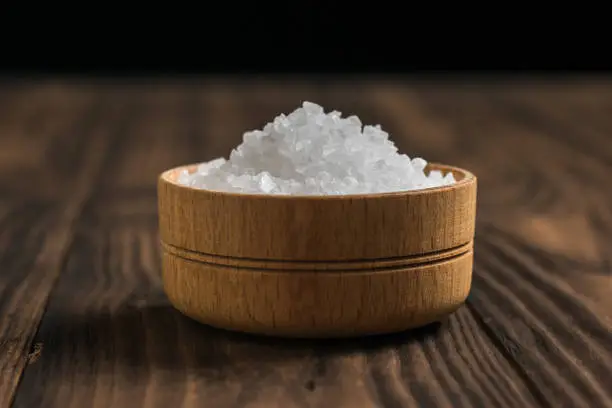 Salt in a wooden saltshaker on a dark rustic table. Ground stone sea salt.