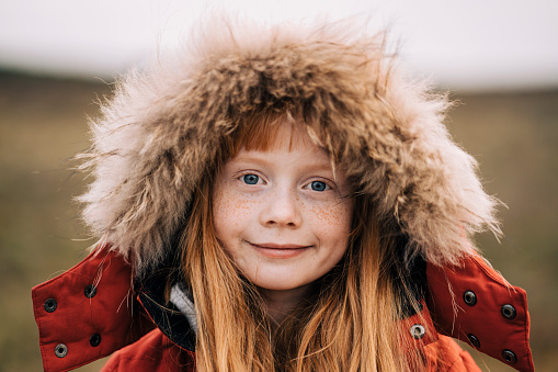 Portrait of cute smiling girl wearing fur hood. Close-up of female child is having freckles. She is standing outdoors.