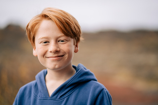 Close-up portrait of smiling blond boy. Cute male child is outdoors during winter. He is wearing blue warm clothing.