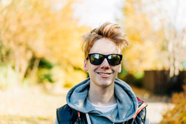 Smiling teenage boy wearing sunglasses at park Portrait of smiling teenage boy wearing sunglasses. Confident male is wearing hood on sunny day. He is standing at park during winter. teenager boy haircuts stock pictures, royalty-free photos & images