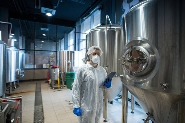 istock Photo of technologist in white protective uniform holding tablet and controlling food production in processing factory. Worker doing quality control. 1198198765