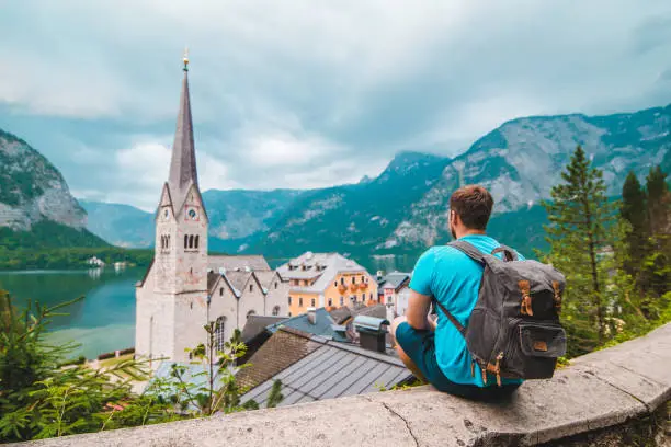 man with backpack sitting and enjoying the vie of hallstatt austria summer travel concept