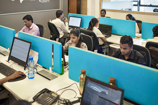 High angle view of young Indian office workers sitting at desks divided by panels and concentrating on their computer work.