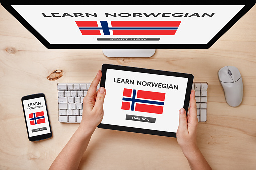 Learn Norwegian concept on computer, tablet and smartphone screen over wooden table. Top view of responsive devices.