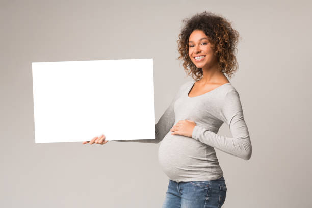 istock Black expectant woman holding blank advertising board 1198210496