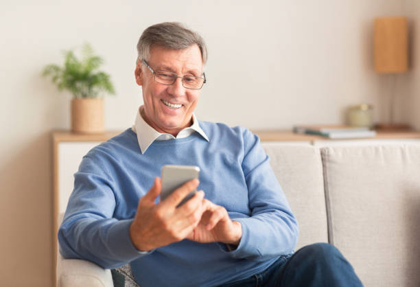 istock Joyful Elderly Man Using Cellphone Sitting On Sofa At Home 1198212228
