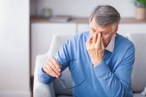 istock Elderly Man Massaging Nosebridge Sitting On Couch Indoor 1198212336