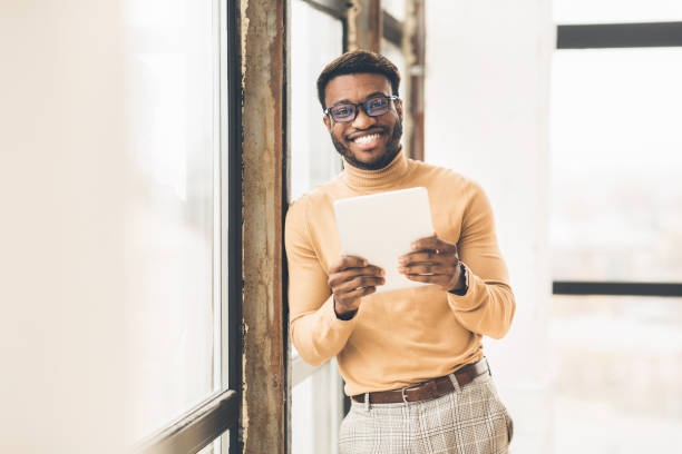 istock Smiling afro businessman using tablet near office window 1198218613