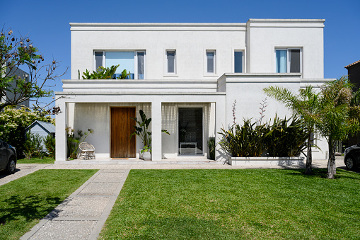 Sunny view of modern two-story home in Buenos Aires with well-tended front yard and walkway leading to entrance.