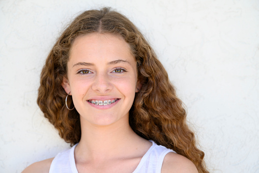 Headshot of cheerful 14 year old Buenos Aires girl with long curly hair wearing white tank top and smiling at camera.