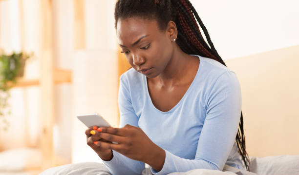 istock Serious Girl Using Cellphone Texting Sitting In Bed At Home 1198218981