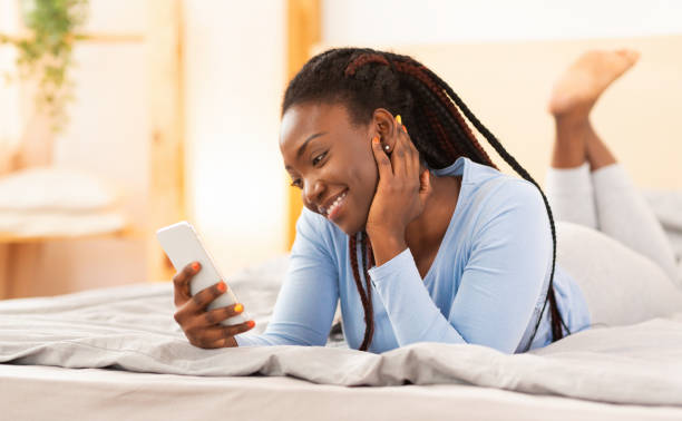 istock Cheerful Afro Woman Using Smartphone Lying In Bed 1198219773