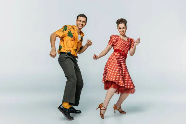 Photo of cheerful dancers looking at camera while dancing boogie-woogie on grey background