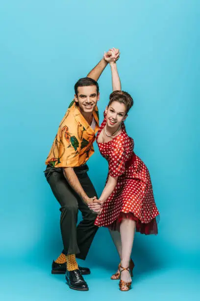 Photo of elegant dancers holding hands while dancing boogie-woogie on blue background