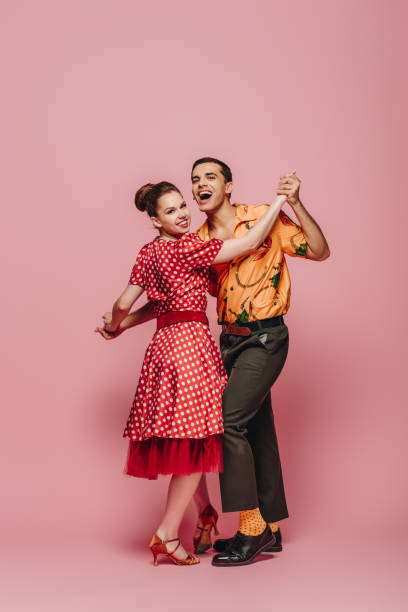 stylish dancers holding hands while dancing boogie-woogie on pink background stylish dancers holding hands while dancing boogie-woogie on pink background boogie woogie dancing stock pictures, royalty-free photos & images