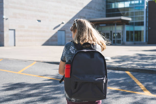 Teen girl/student walking to her school in the morning while wearing a backpack and holding binders. stock photo