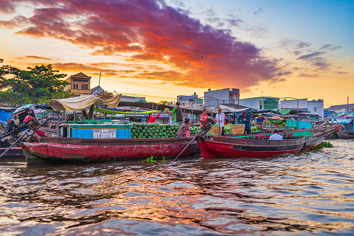 Can Tho, Vietnam - january 7, 2020: Cai Rang floating market at sunrise, boats selling wholesale fruits and goods on Can Tho River, Mekong Delta region, South Vietnam, tourism destination. Dramatic sky sunburst