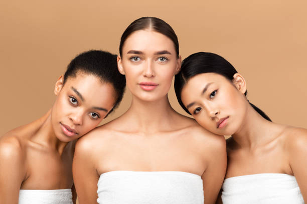 Three Girls Wrapped In Towels Posing Over Beige Background Body Care. Three Diverse Girls Models Wrapped In Towels Posing Looking At Camera Over Beige Background. Studio Shot diverse models stock pictures, royalty-free photos & images