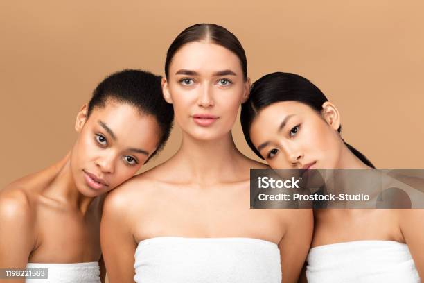 Three Girls Wrapped In Towels Posing Over Beige Background Stock Photo - Download Image Now