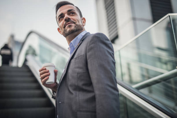 istock Businessman with disposable cup riding on escalator in city 1198222697