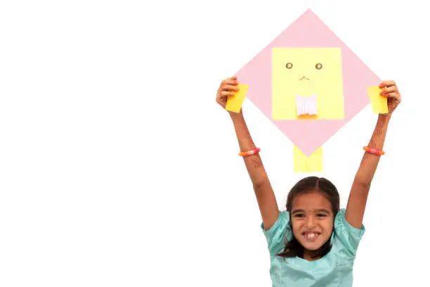 Young Indian village traditional girl with excitement holding kite over isolated background - concept of kids playing kites during Sankranti festival
