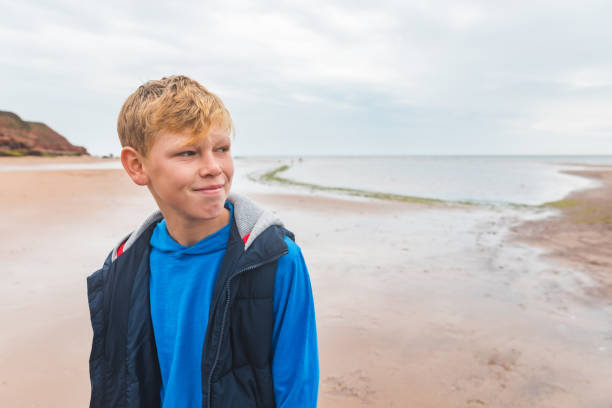 Boy alone portrait on the beach on cloudy day - Kid with blond hair alone at seaside looking away from camera