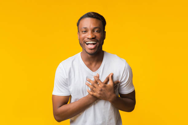 African American Man Laughing Touching Chest Standing Over Yellow Background
