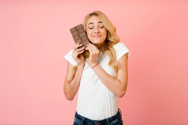 Pretty millennial woman hugging chocolate bar, pink background