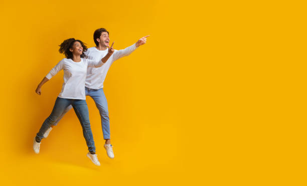 istock Multiracial couple pointing at copy space and jumping over yellow background 1198225764