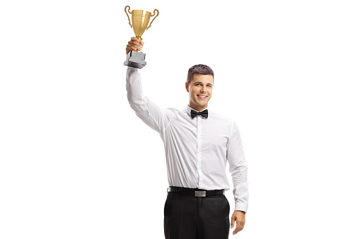 Full length portrait of a young man in a tux holding a golden trophy isolated on white background