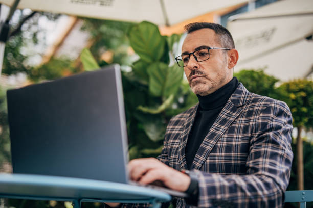 istock Businessman using laptop in sidewalk cafe 1198227129
