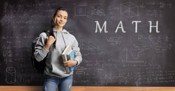 istock Female student with books and backpack standing in front of a blackboard with math formulas 1198227300