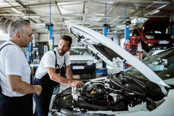 istock Auto mechanics communicating while examining car engine in auto repair shop. 1198227302