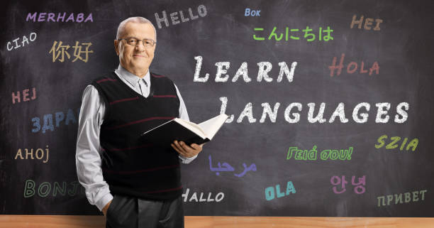 mature male teacher in front of a blackboard with hello written in different foreign languages - spanish culture teacher learning text imagens e fotografias de stock