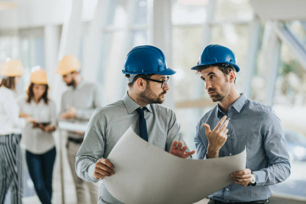 istock Two male architects talking while examining blueprints in the office. 1198228429