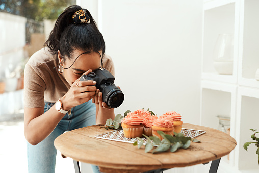 Cropped shot of an attractive young businesswoman using her camera to photograph cupcakes for her blog
