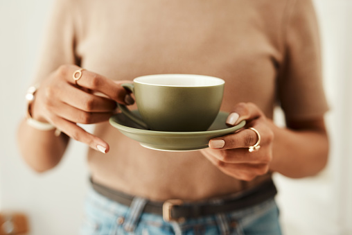 Cropped shot of an unrecognizable woman standing alone in her home and holding a cup of coffee