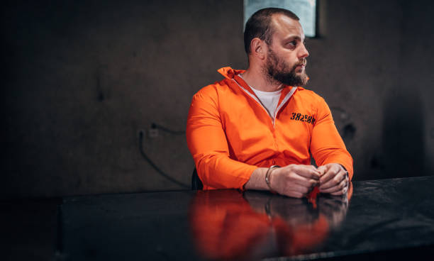 istock Prisoner in orange jumpsuit sitting alone in interrogation room 1198229391