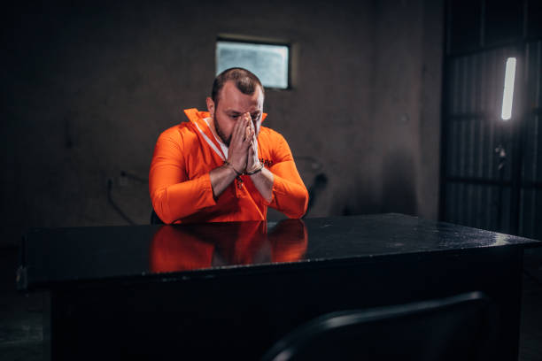 istock Prisoner in orange jumpsuit sitting alone in interrogation room 1198229610